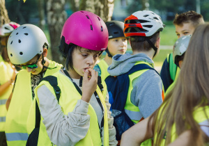 Grupa uczniów w żółtych kamizelkach i kaskach przygotowuje się do wycieczki rowerowej.